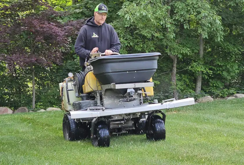 An Ecolawn technician on a ride-on spreader in a backyard